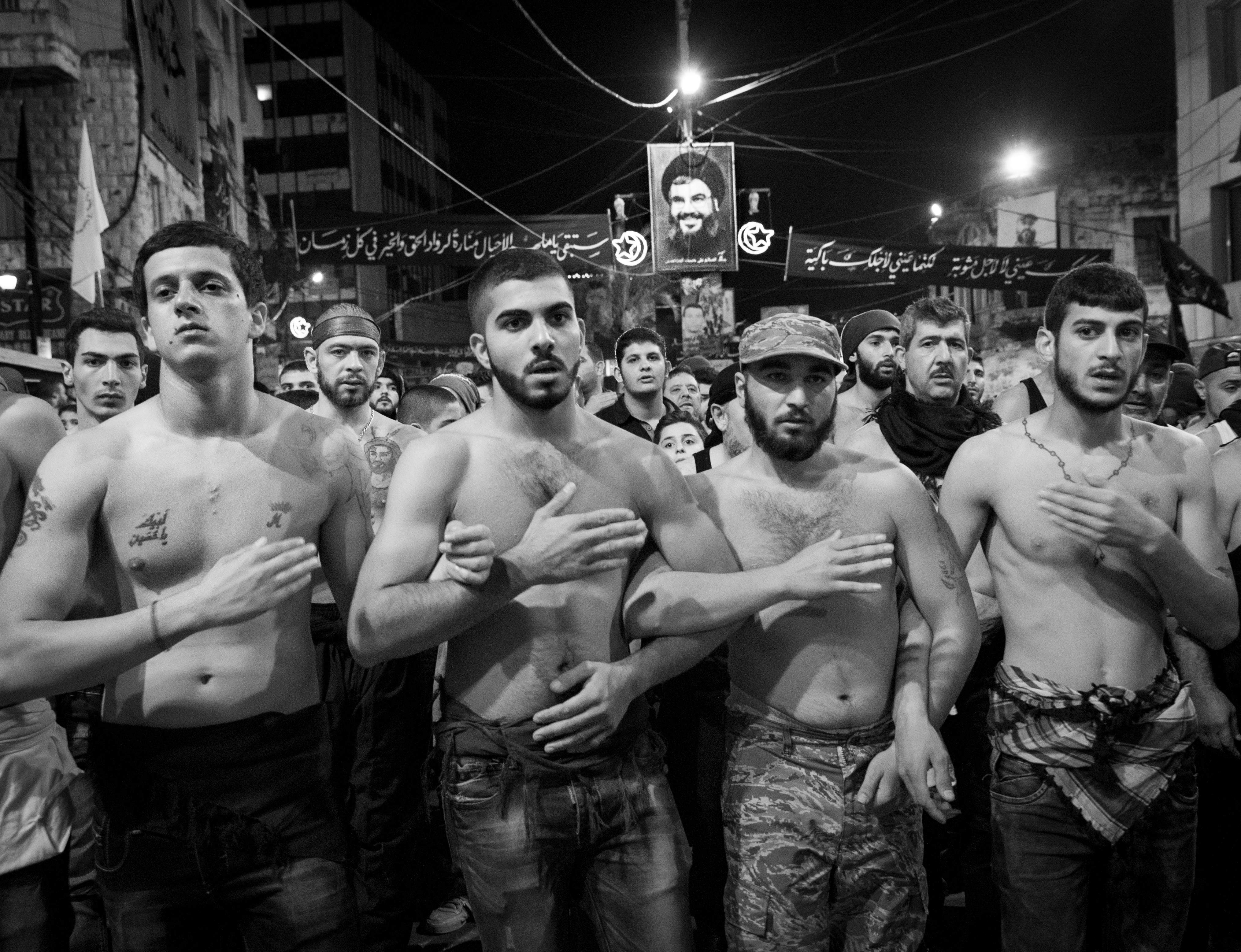 Young Shia men pounding their chests beneath a poster of Hezbollah's leader, Hassan Nasrallah, Nabatiyeh, Lebanon, November 2014 (photo: Maya Hautefeuille)