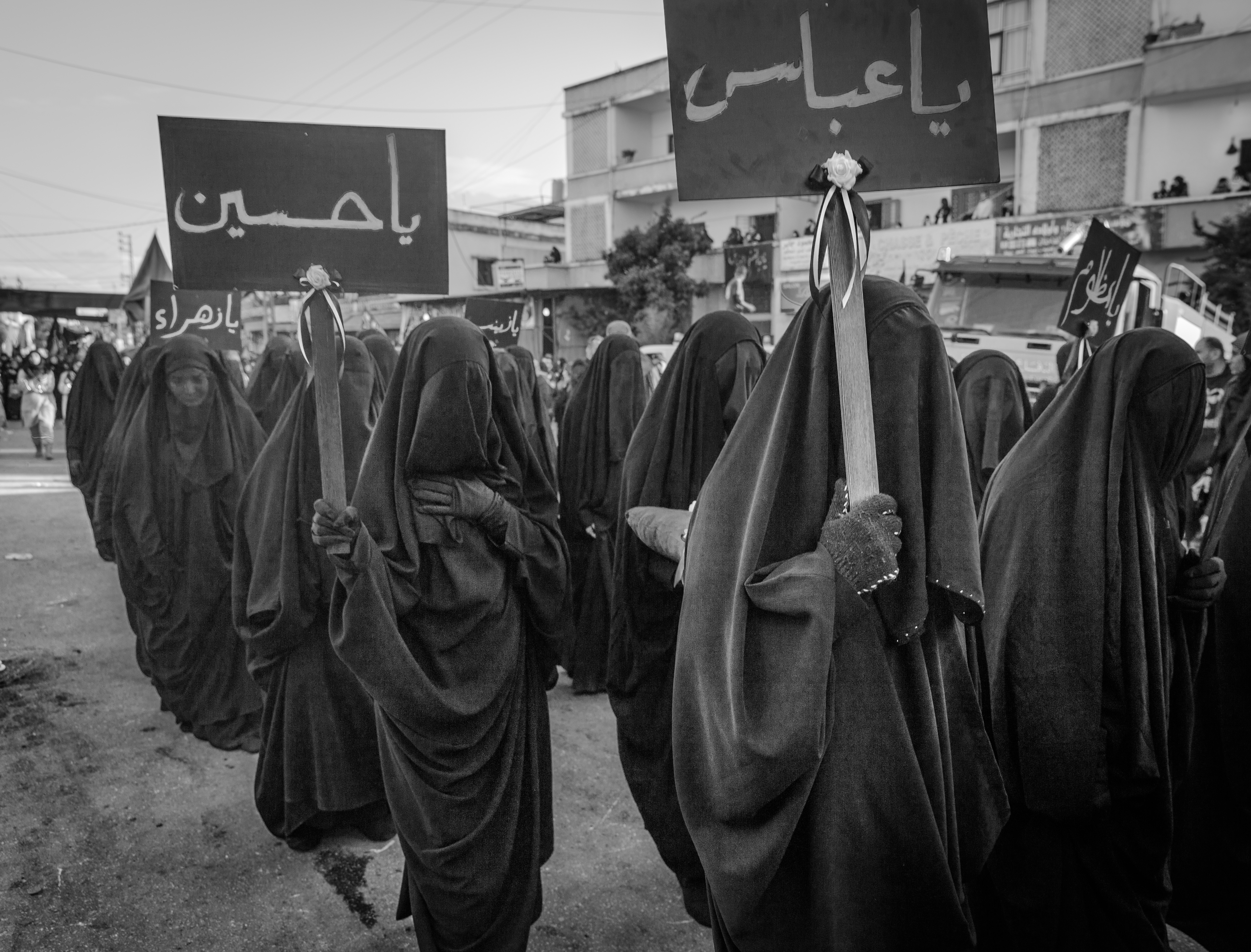 Veiled Shia women carry signs with the names of Ali and Hussein through the streets of Nabatiyeh, Lebanon, November 2014 (photo: Maya Hautefeuille)