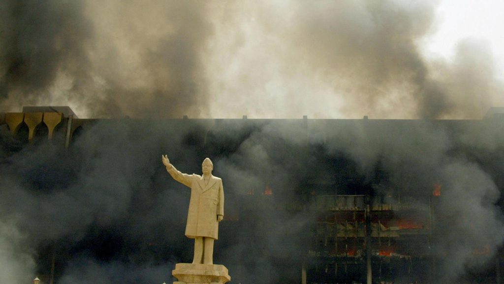 Saddam-Statue vor dem brennenden Irakischen Olympischen Komitee in Bagdad am 9. April 2003; Foto: AFP/picture-alliance 