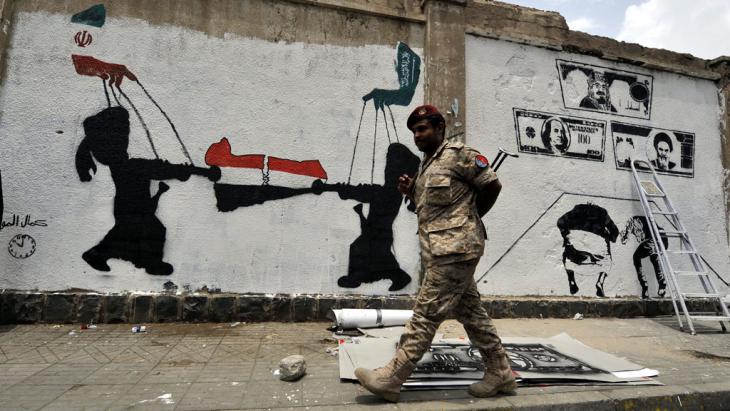 A soldier walks past a wall covered in graffiti indicating the influence of Iran and Saudi Arabia on Yemen (photo: picture-alliance/epa/Y. Arhab)