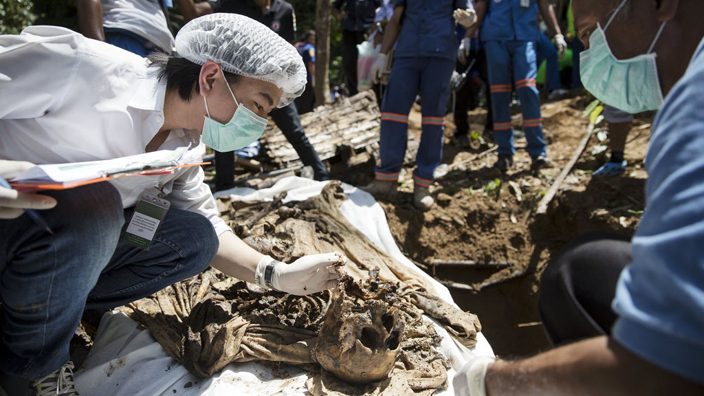 A forensic expert inspects human remains found in a mass grave in Thailand (photo: Reuters/D. Sagolj)