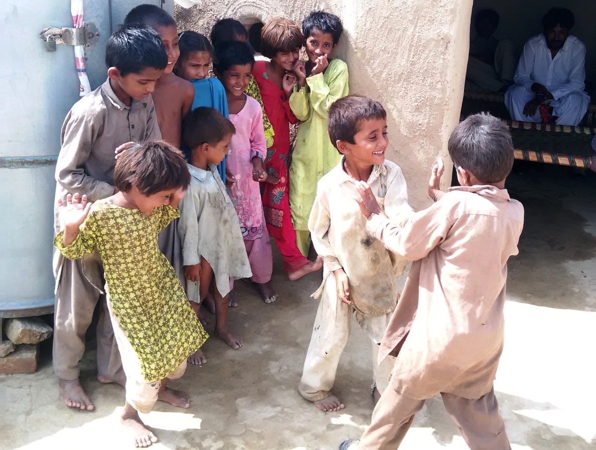 Kinder stehen nebeneinander, während zwei Jungen vor ihnen miteinander kämpfen. Foto: Usman Mahar