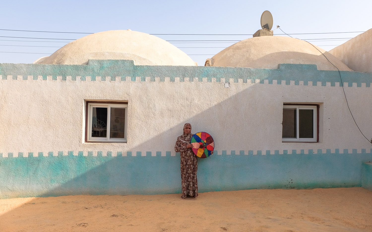 A West Aswan woman holding a ″tegiddy″ stands in front of her new extension (photo: Maya Hautefeuille)