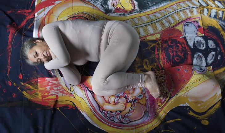 An elderly participant in the photo project lies in the foetal position on a painted background (photo: Heba Khalifa)