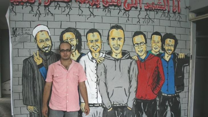 Ahmed Maher stands in front of revolution graffiti in Cairo (photo: Markus Symank)