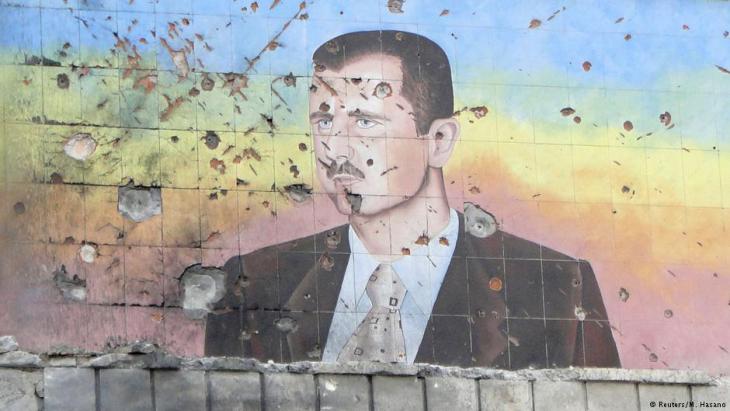 Shrapnel-scarred and pockmarked facade of a police building in Aleppo bearing a likeness of Assad (photo: Reuters)