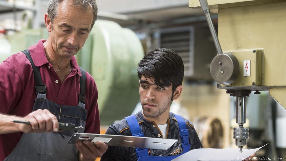 Trainer Wolfgang Wonneberger (l) from Jenaer Feinblech GmbH in Jena, Thuringia demonstrates working techniques to 19-year-old Afghan refugee Rezwan Waziri, 25.08.2016 (photo: picture-alliance/dpa/J.-U. Koch)