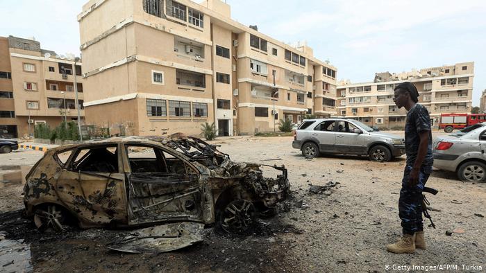 A man stands with a gun next to a burnt-out car in Tripoli (photo: Getty Images/AFP/M. Turkia)
