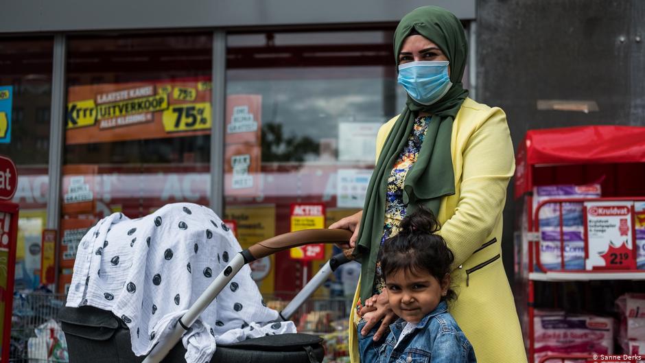 A woman in a headscarf and medical face mask pushes a pushchair holding her daughter's hand (photo: Sanne Derks)