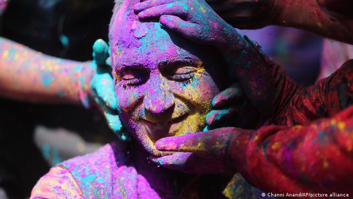 People touch the face of a man covered in coloured powder (photo: Channi Anand/AP/picture-alliance)