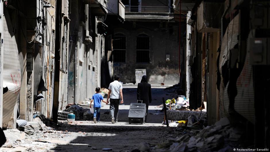 Members of a family walk past damaged buildings as they head to inspect their home in the Wadi Al-Sayeh district at the al-Khalidiyeh area in Homs, 14 May 2014 (photo: Reuters/Omar Sanadiki)