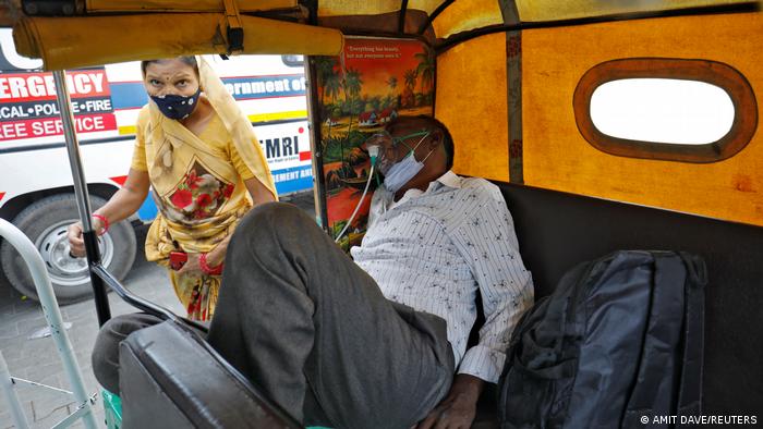 A patient wearing an oxygen mask waits inside an auto rickshaw to enter a COVID-19 hospital for treatment