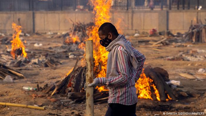 A man walks past burning funeral pyres of people who died of COVID-19 at a crematorium ground in New Delhi