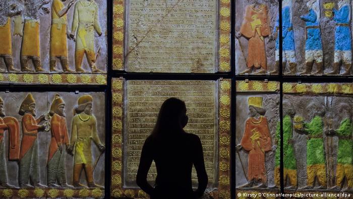 A museum staff member in shadow looks at a colour projection ahead of the 'Epic iran' exhibition