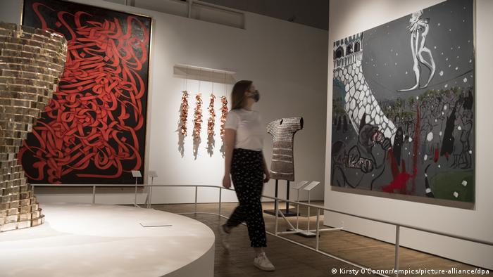 A museum staff member walks past two large-scale artworks, one with a black background and red, ribbon-like strokes and one black-and-white painting splotted with red at the 'Epic Iran' show