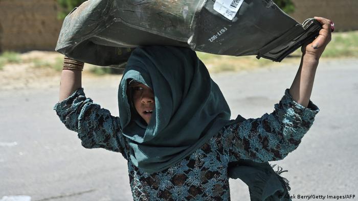A girl picks up a dented metal box from the scrap yard in Bagram