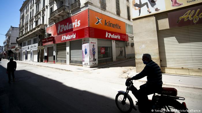 Street with closed shops, empty but for one man on a motorcycle and a pedestrian (photo: Yassine Gaidi/AA/picture-alliance)