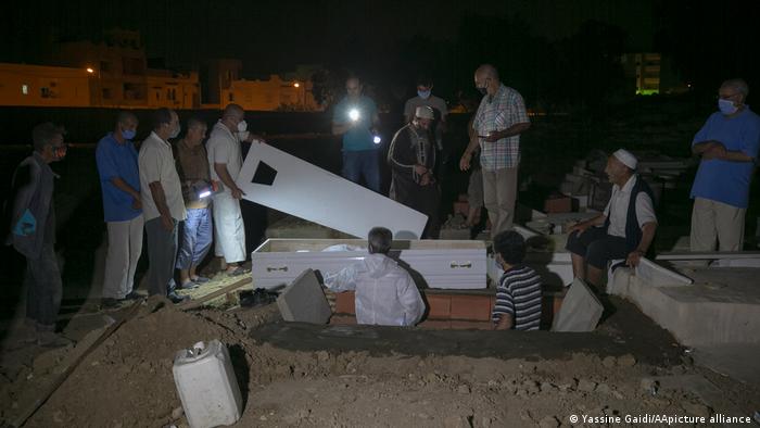 Men in a graveyard in the dark, one holding the lid of a coffin (photo: Yassine Gaidi/AA/picture-alliance)
