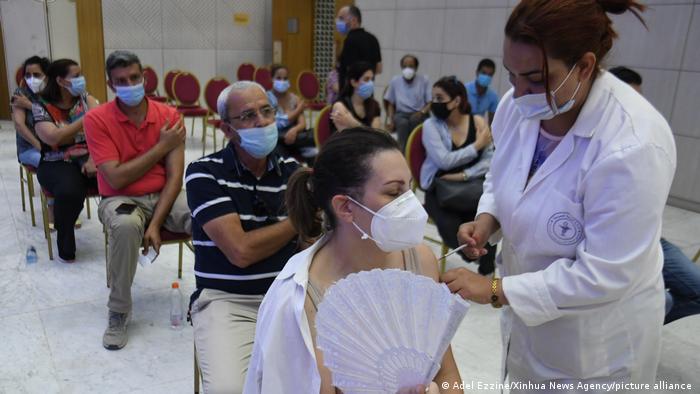 People sitting on chairs and wearing face masks, a woman in the foreground in being vaccinated by another woman (photo: Adel Ezzine/Xinhua News Agency/picture-alliance)