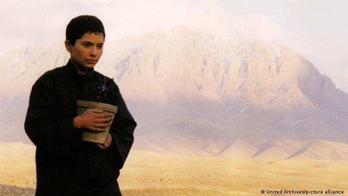 A young person holding a bucket in a mountainous desert landscape