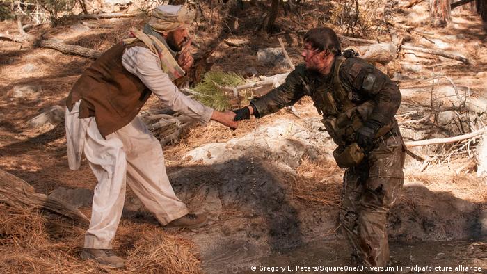 A bloodied US Navy SEAL holds the hand of a man in traditional Afghan dress, who is gesturing him to keep quiet