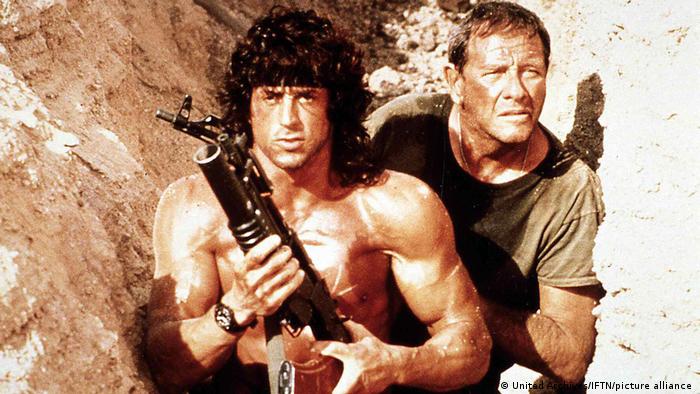 Rambo with a weapon and his friend in a cleft in a rockface