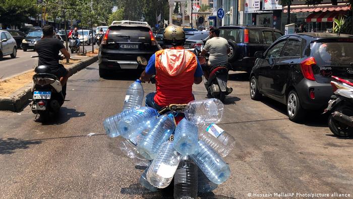 A man on a moped transports empty plastic water bottles.