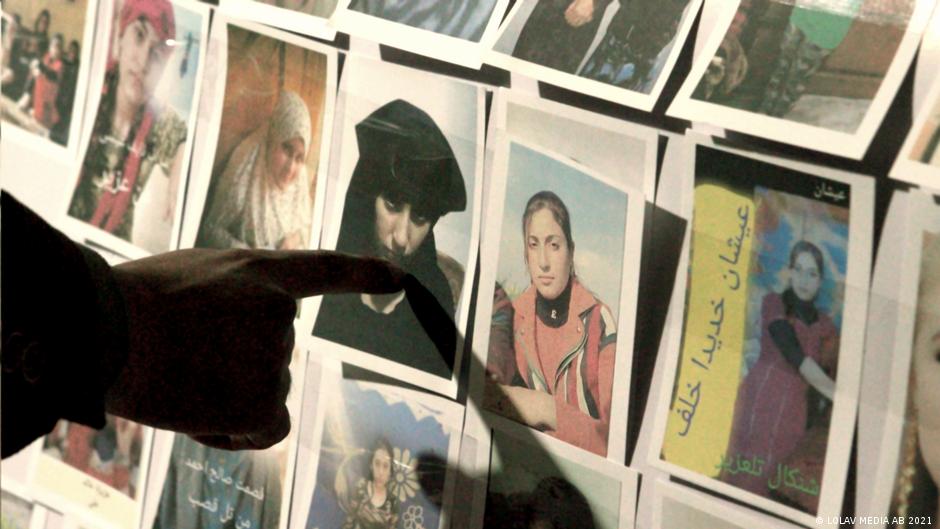 Still from "Sabaya": A finger pointing the picture of a girl among several; these are all photos of missing Yazidi girls
