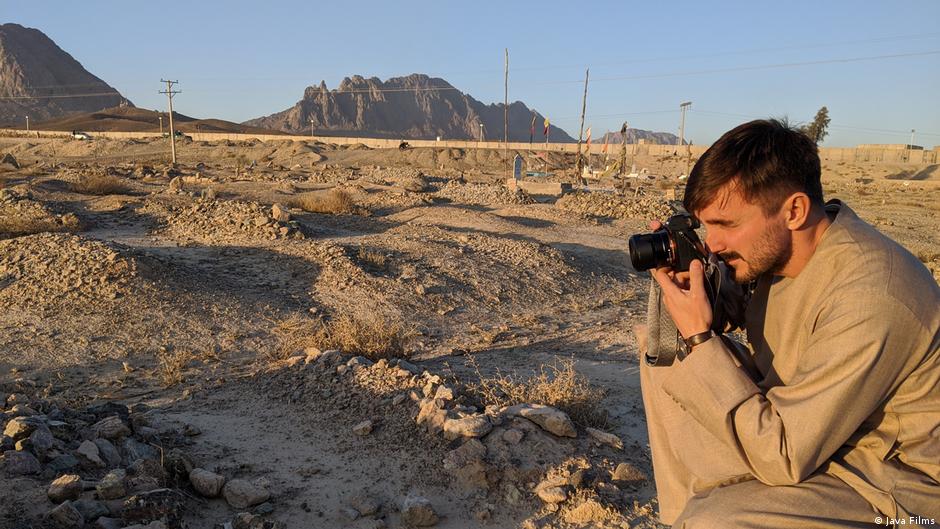 Still from "Ghosts of Afghanistan": a man taking photos in a desert landscape that serves as a graveyard