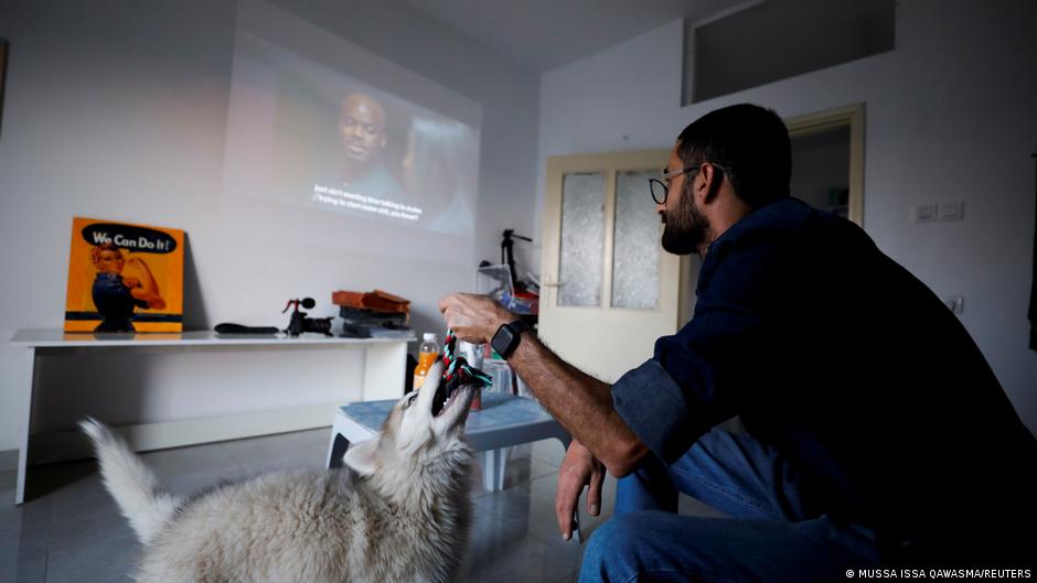 Palestinian Abdallah Maraka plays with his dog while he watches a series on Netflix in his house in Hebron, in the Israeli-occupied West Bank, 14 October 2021 (photo: Reuters/Mussa Qawasma)