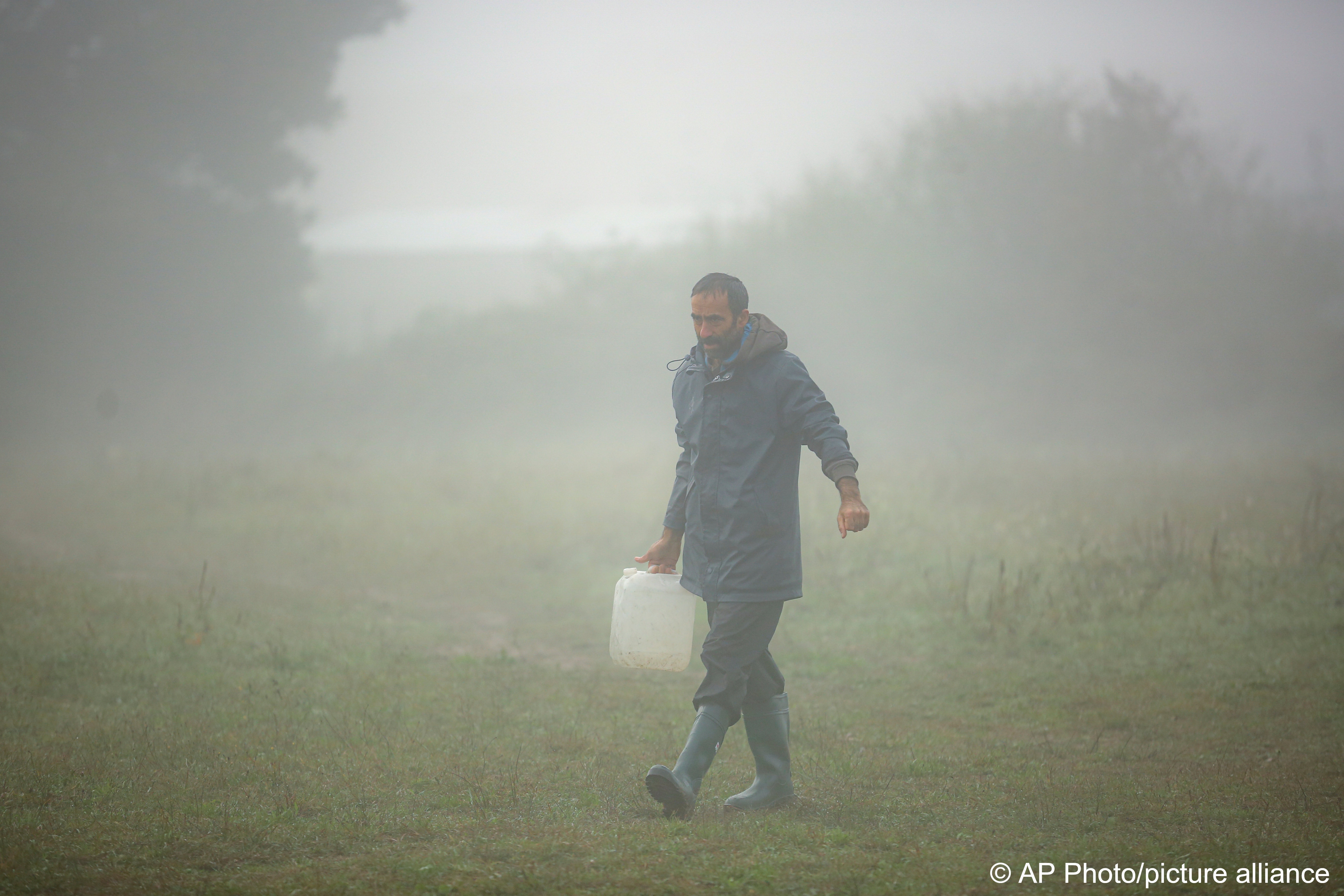 A migrant man carries drinking water on a foggy morning at a makeshift camp housing migrants mostly from Afghanistan, in Velika Kladusa, Bosnia, 12 October 2021 (photo: AP Photo)