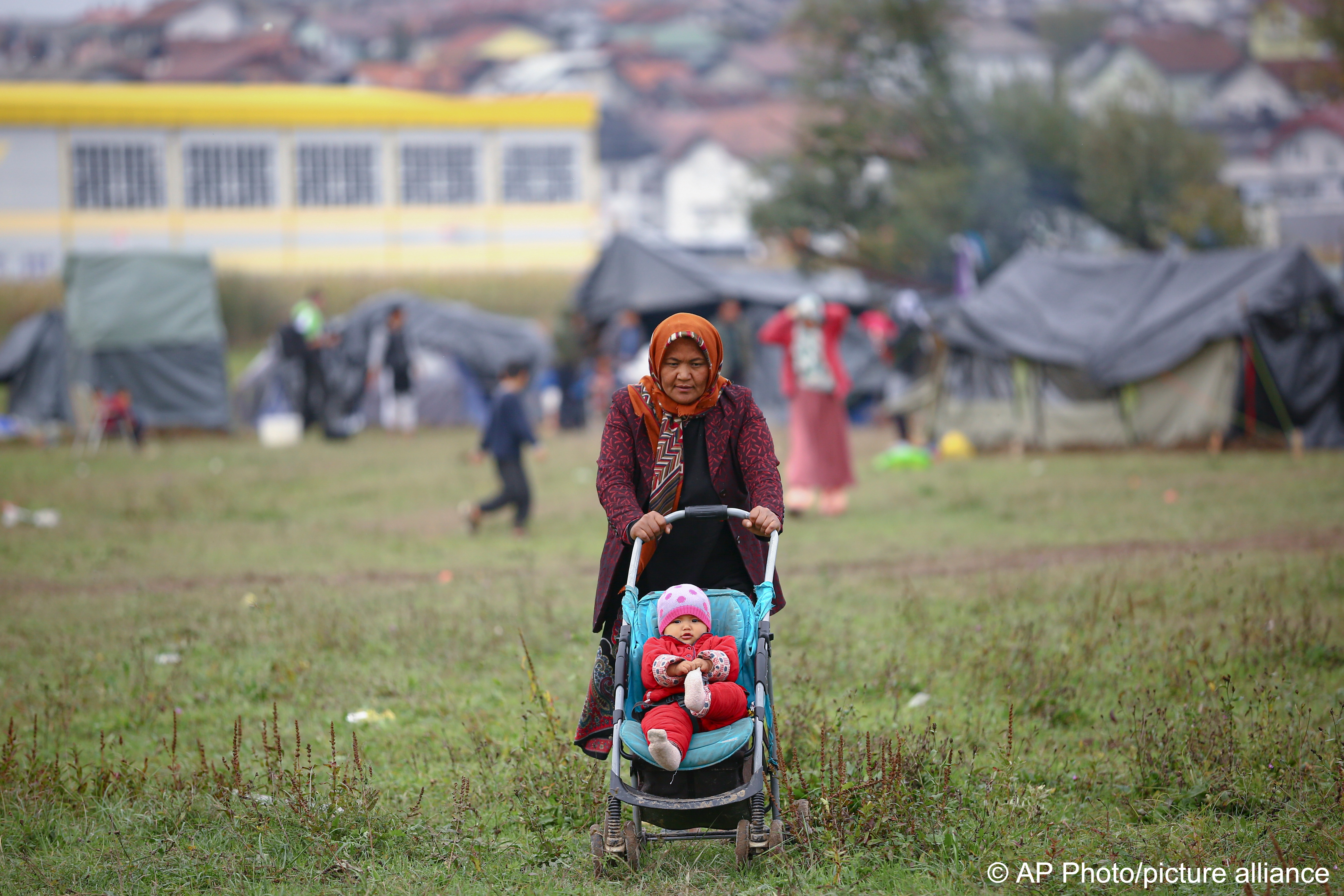 A migrant woman pushes a baby stroller at a makeshift camp housing migrants mostly from Afghanistan, in Velika Kladusa, Bosnia, 12 October 2021 (photo: AP Photo)