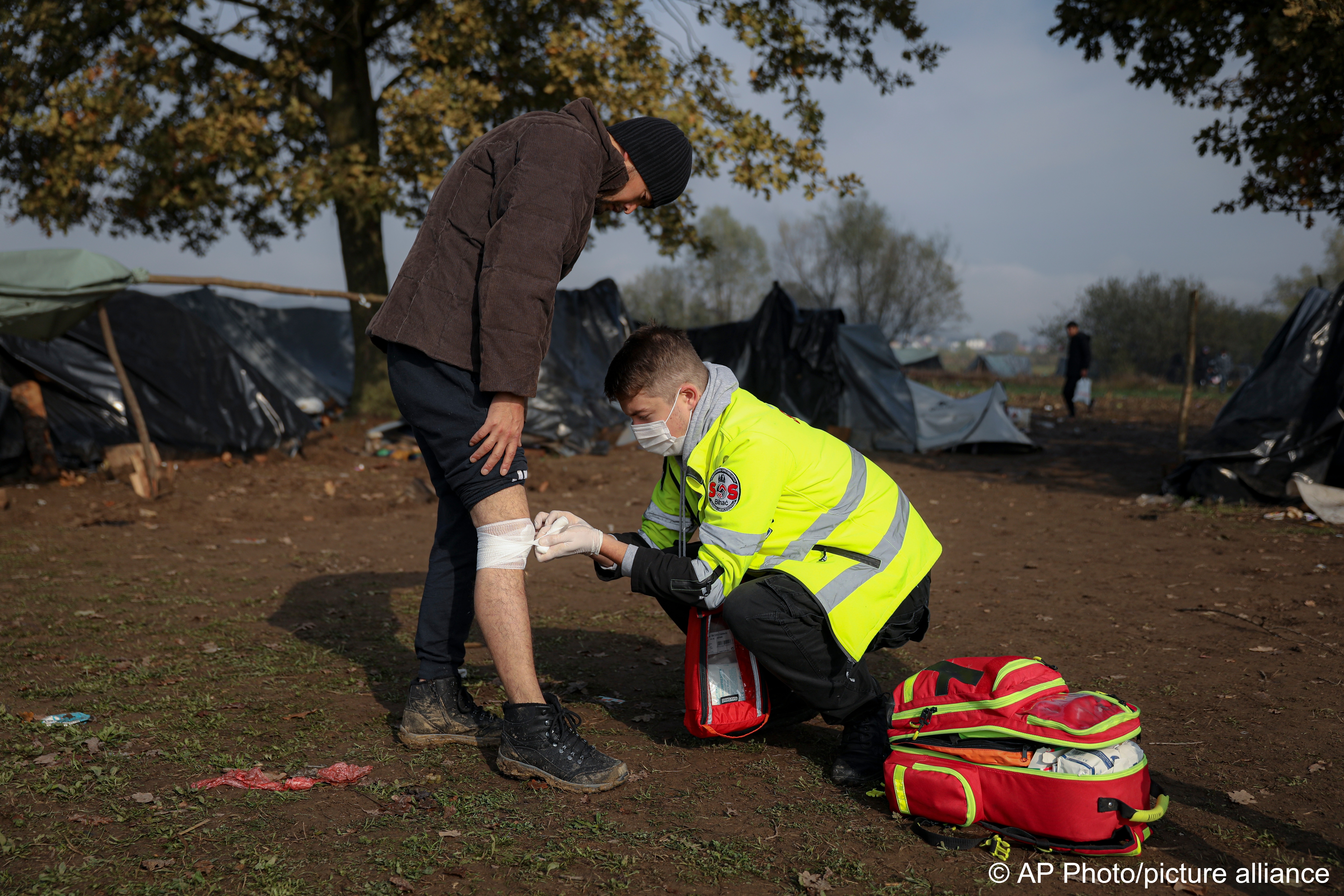 A volunteer of the SOS Bihac NGO looks after an injured migrant at a makeshift camp housing migrants mostly from Afghanistan, in Velika Kladusa, Bosnia, 12 October 2021 (photo: AP Photo)