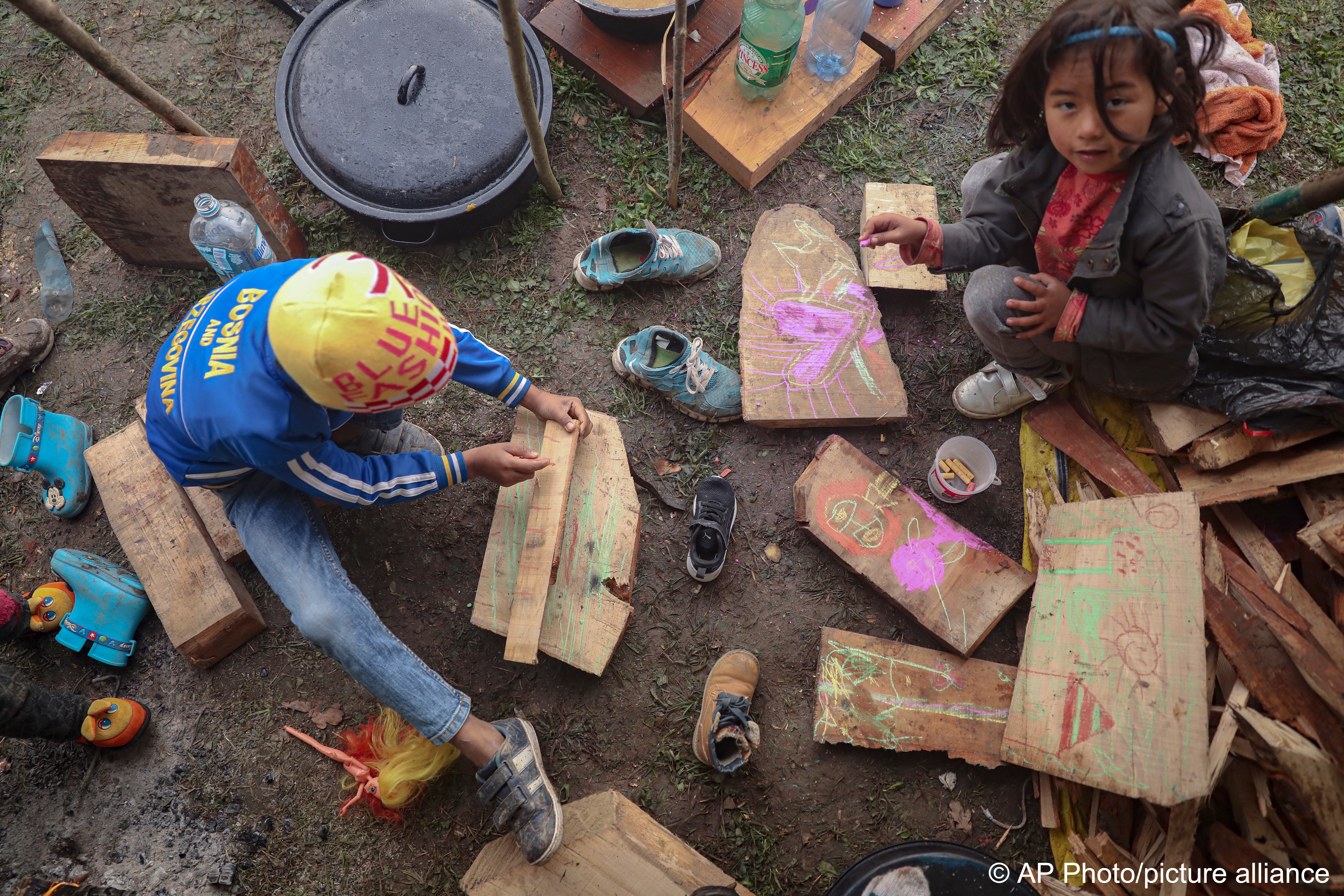Migrantenkinder malen auf Holzstücken in einem Behelfslager für Migranten, die hauptsächlich aus Afghanistan stammen, in Velika Kladusa, Bosnien, 12. Oktober 2021; Foto: AP Photo