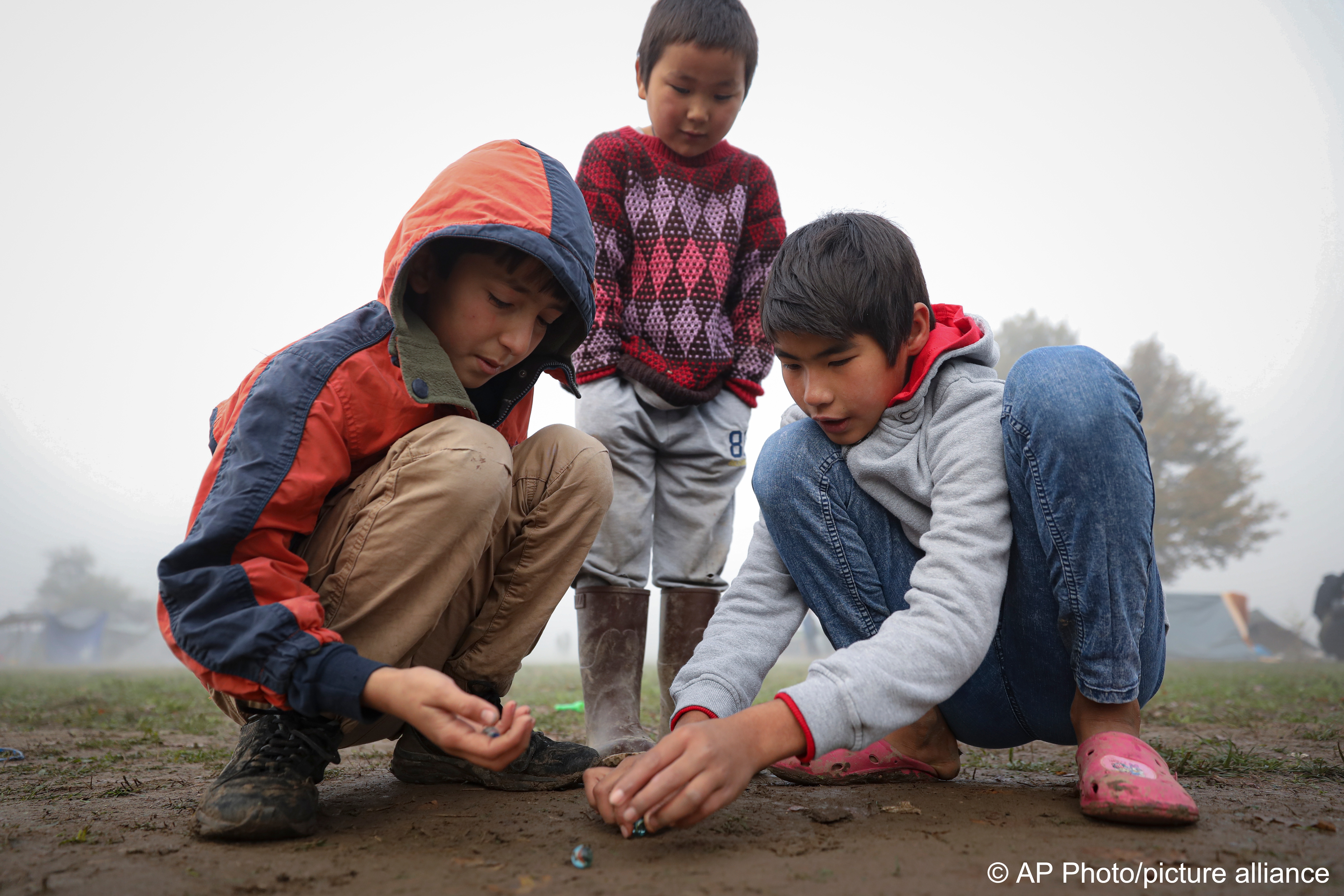 Migrantenkinder spielen mit Murmeln in einem Behelfslager für Migranten, die hauptsächlich aus Afghanistan stammen, in Velika Kladusa, Bosnien, 12. Oktober 2021; Foto: AP Photo 