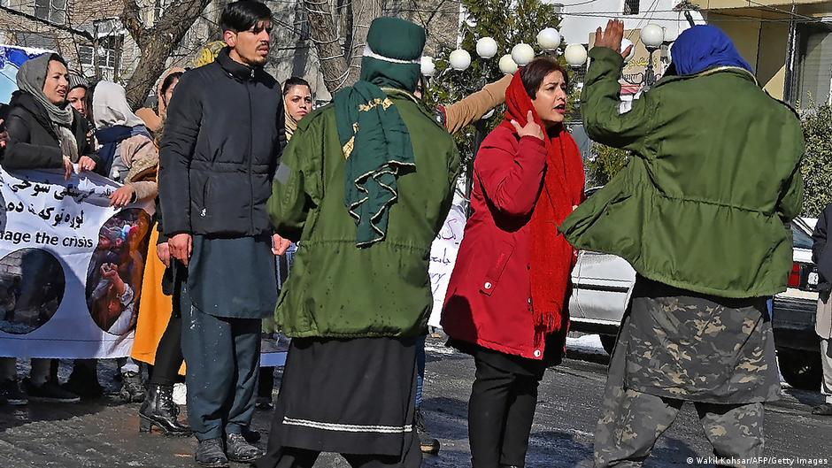 امرأة تخاطب أحد أفراد مسلحي طالبان بينما تحمل نساء لافتة بينما تنظر إليها نساء أخريات.