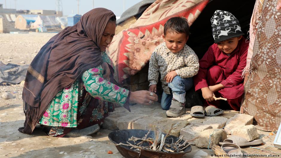 تحملت المرأة الأفغانية في المناطق الريفية ويلات استمرار المعارك والقتال مع ارتفاع معدلات الفقر. A woman and two children watch a small fire outside a tent (photo: Sayed Khodaiberdi Sadat/AA/picture alliance)
