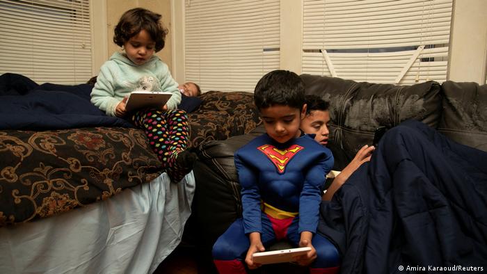 Siblings Sanaullah Khan Zadran, 6, dressed up as Superman, Zahra Zadran, 4, and his brother Samiullah Khan Zadran, 13, play on their tablets