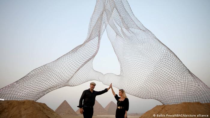 Italian artists pose under their installation facing the pyramids on the Giza plateau on 23 October 2021