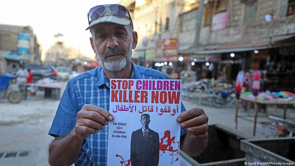 رجل سوري يحمل ملصقاً يقول إن الرئيس السوري بشار الأسد قاتل.