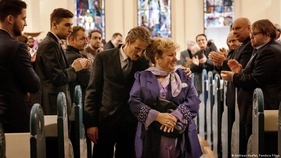 A still in which mother and lawyer walk down an aisle as people clap for them (photo: Andreas Hoefer/Pandora Films)
