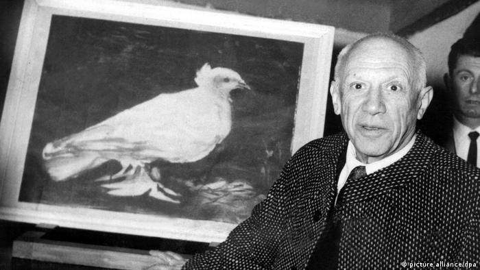 Pablo Picasso stands in front of his famous lithograph of the white dove