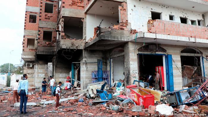 Menschen stehen inmitten von Trümmern am Ort eines tödlichen Autobombenanschlags in der Nähe eines Sicherheitskontrollpunkts außerhalb des internationalen Flughafens von Aden im Stadtteil Khormaksar