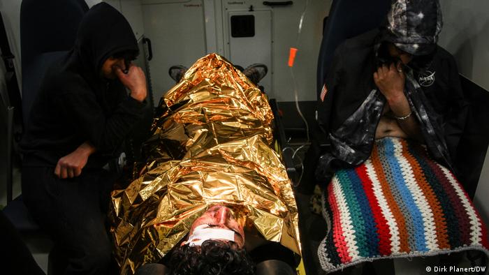 A man lies with his head towards the camera. He is wrapped in a golden metal foil