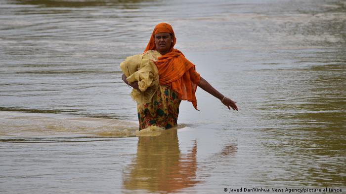 A woman walks through waist-deep water with a bundle tucked under her arm