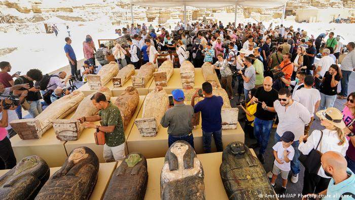 Members of the press stand around the coffins presented by the Egyptian researchers in Giza