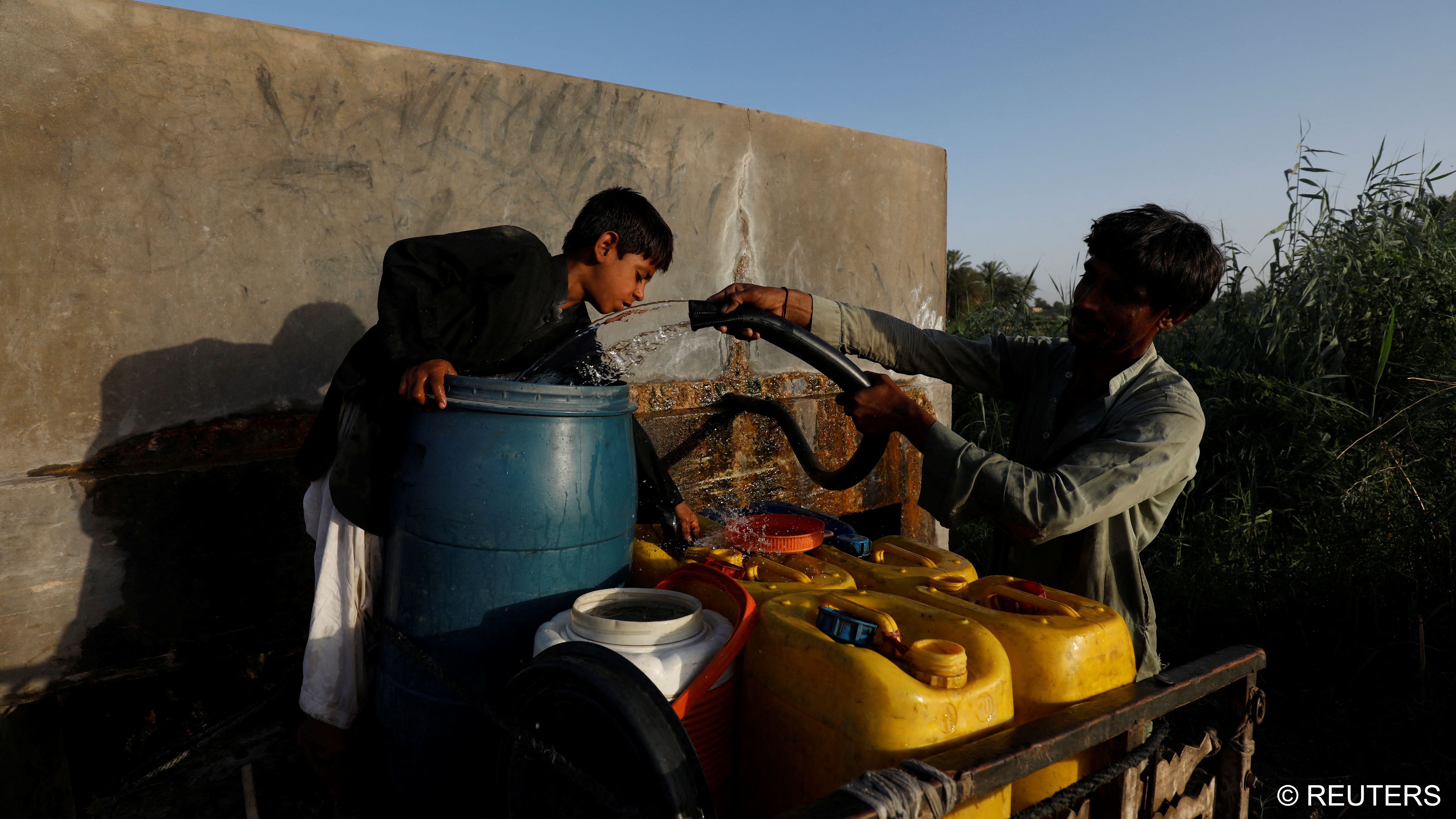A father and his son fill water canisters from a private pump to sell door-to-door (photo: Reuters/Akhtar Soomro)