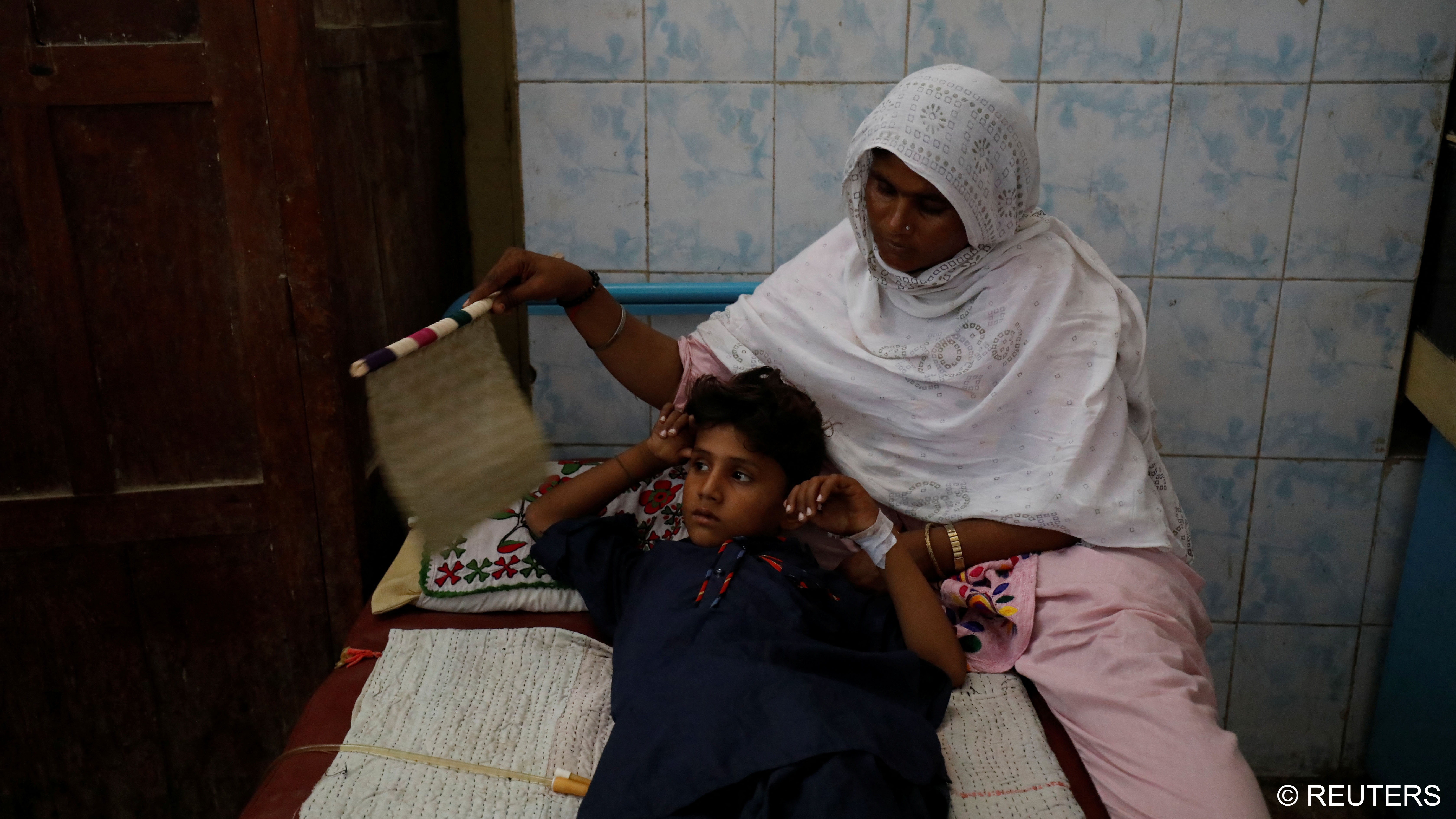 Rabia fans her son, Manish Kumar, 10, as he lies in bed after having a bladder stone removed (photo: Reuters/Akhtar Soomro) 