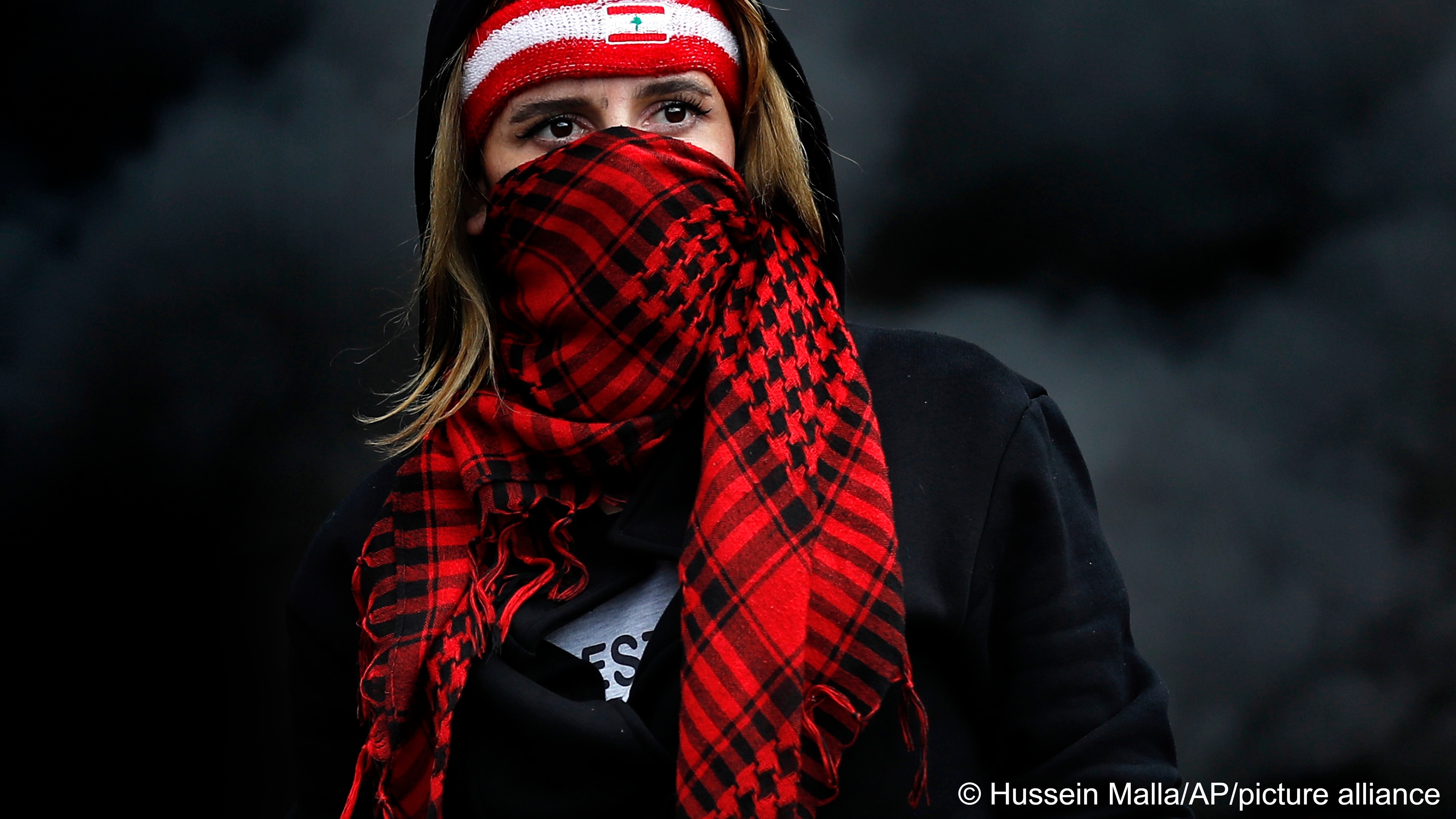 A protester covers her face with a scarf as she blocks a main highway during a protest against the increase in prices of consumer goods and the crash of the local currency, in the town of Zouk Mosbeh, north of Beirut, Lebanon, 8 March 2021 (photo: AP Photo/Hussein Malla)