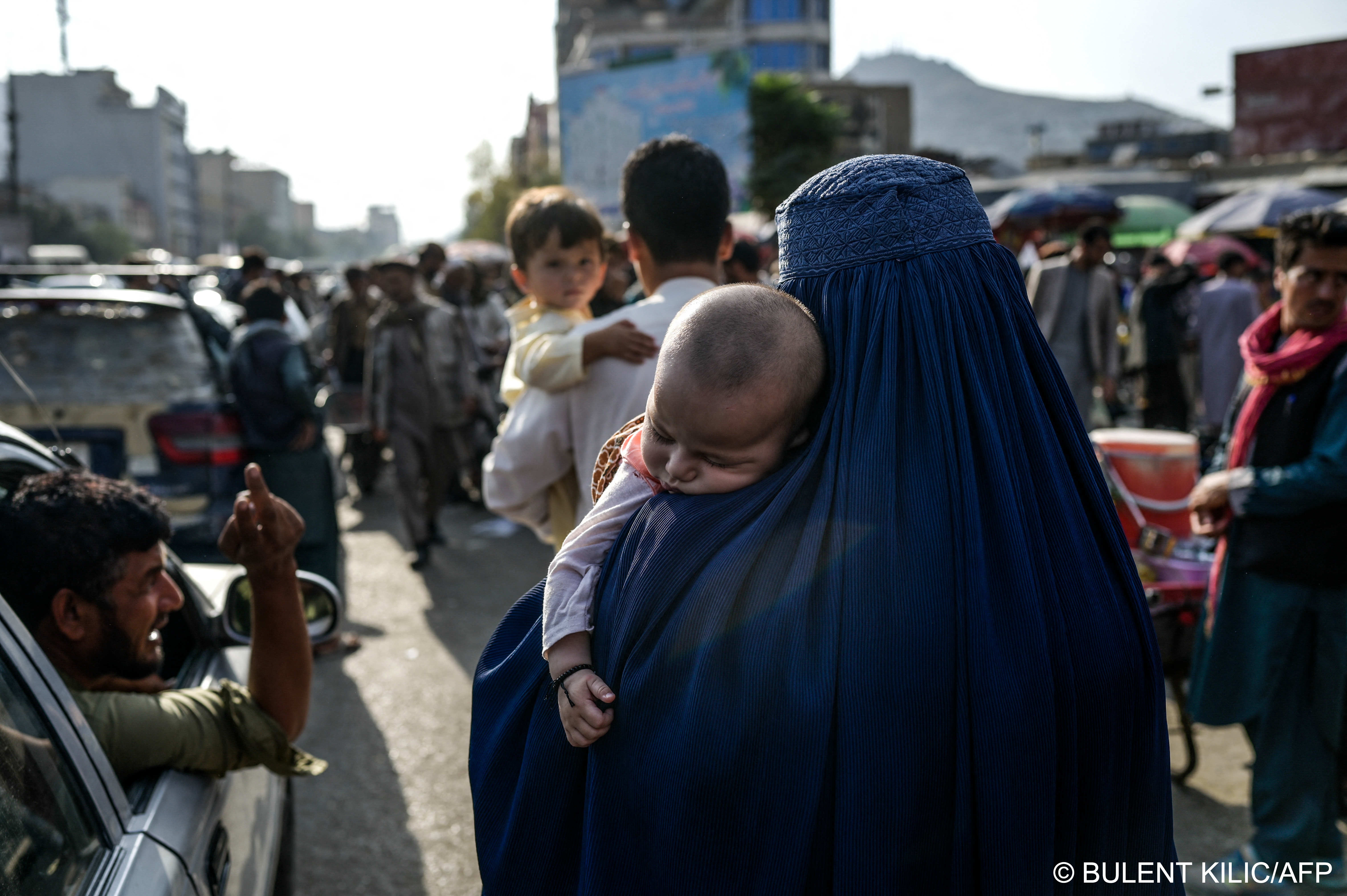 Afghan mother carries infant in crowded street (photo: AFP)